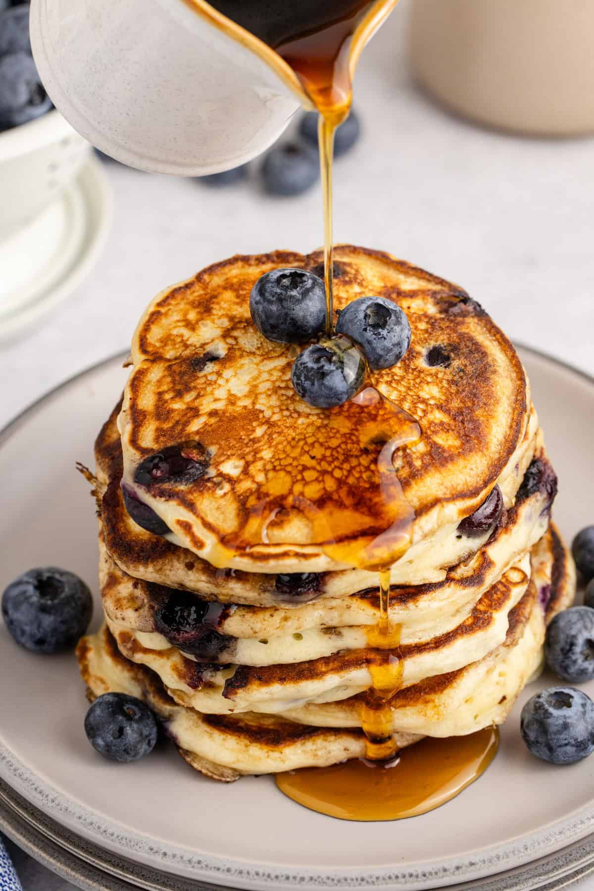 Blueberry Buttermilk Pancakes Stacked on a Plate With Maple Syrup