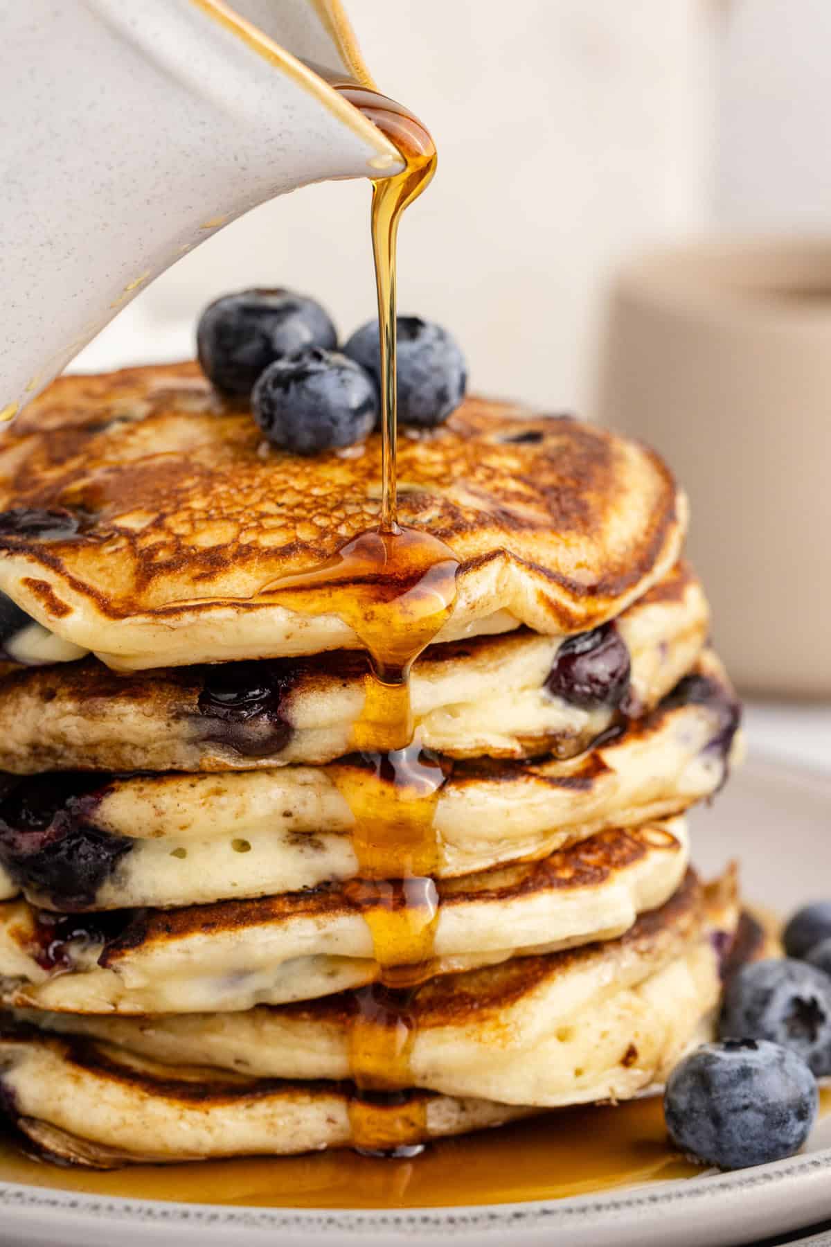 Blueberry Buttermilk Pancakes Piled on a Plate with Syrup Pouring