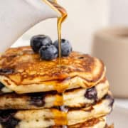 Blueberry Buttermilk Pancakes Piled on a Plate with Syrup Pouring