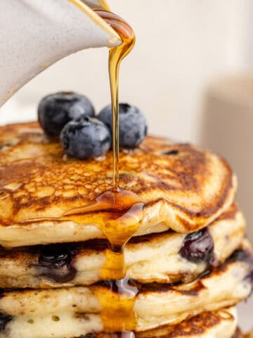 Blueberry Buttermilk Pancakes Piled on a Plate with Syrup Pouring