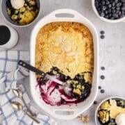 Lemon Blueberry Dump Cake with a Scoop out and Bowls in the back