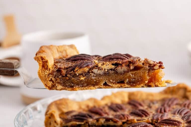 A slice of pecan pie being lifted from a glass pie dish, showcasing a golden crust and rich filling adorned with whole pecans.