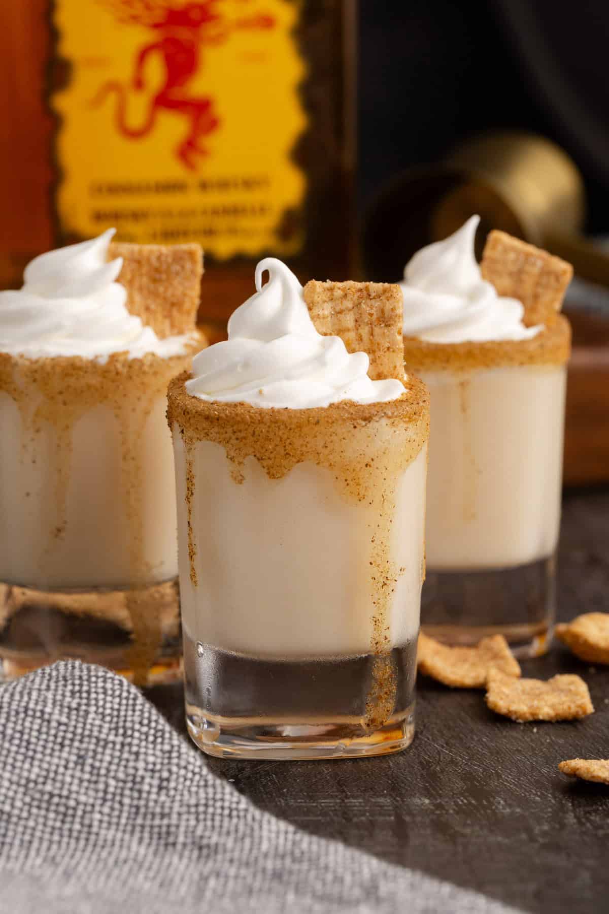 Cinnamon Toast Crunch Shots on a table with Golden Grahams and whipped cream garnish