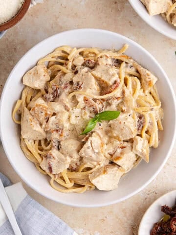 Creamy Sun Dried Tomato Chicken Pasta plated with fresh basil
