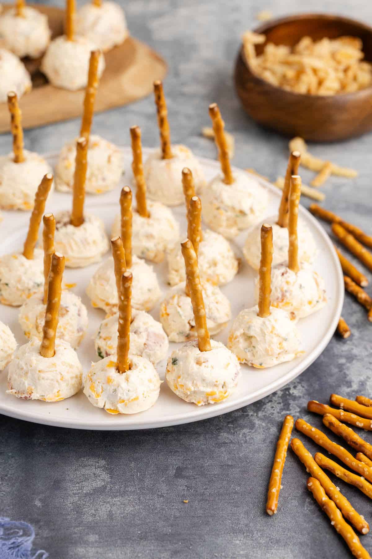 Mini Cheese Balls on a plate with pretzels beside and more on a tray in the back