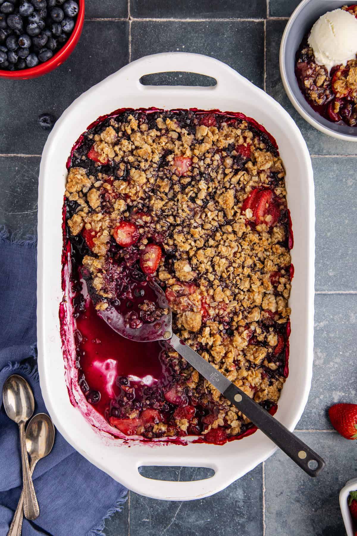 Mixed Berry Crisp with Frozen Berries baked in a casserole dish with a serving spoon