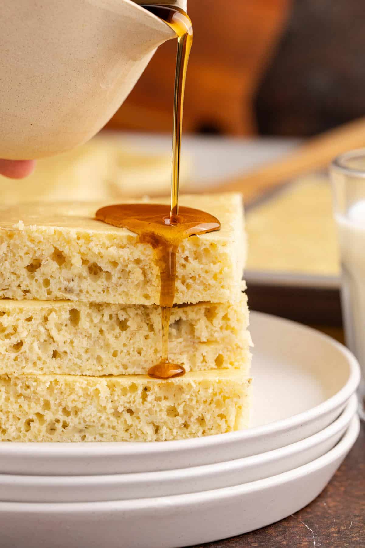 Sheet Pan Banana Pancakes stacked close up with syrup being poured