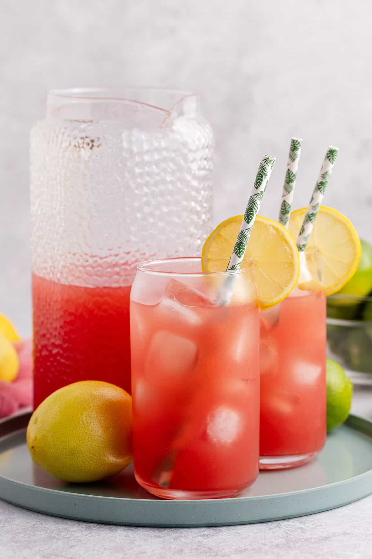 Watermelon Juice Served in Glass Over Ice with Lemon Slice on Tray with Pitcher