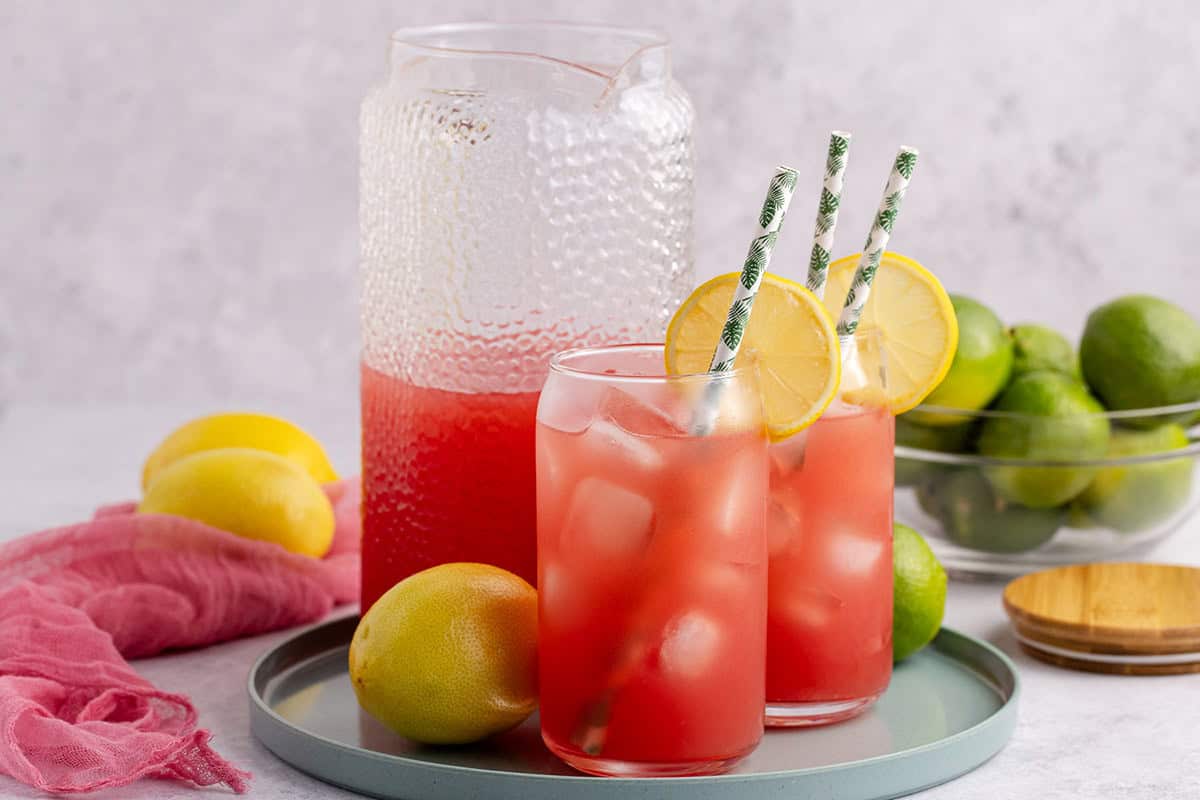 Watermelon Juice Served in Glass Over Ice with Lemon Slice on Tray with Pitcher