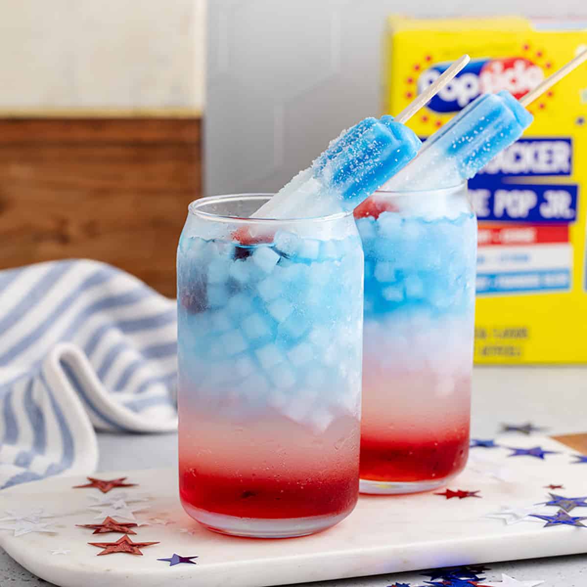 Bomb Pop Cocktail with a Popscile as a garnish on a cutting board with stars all around