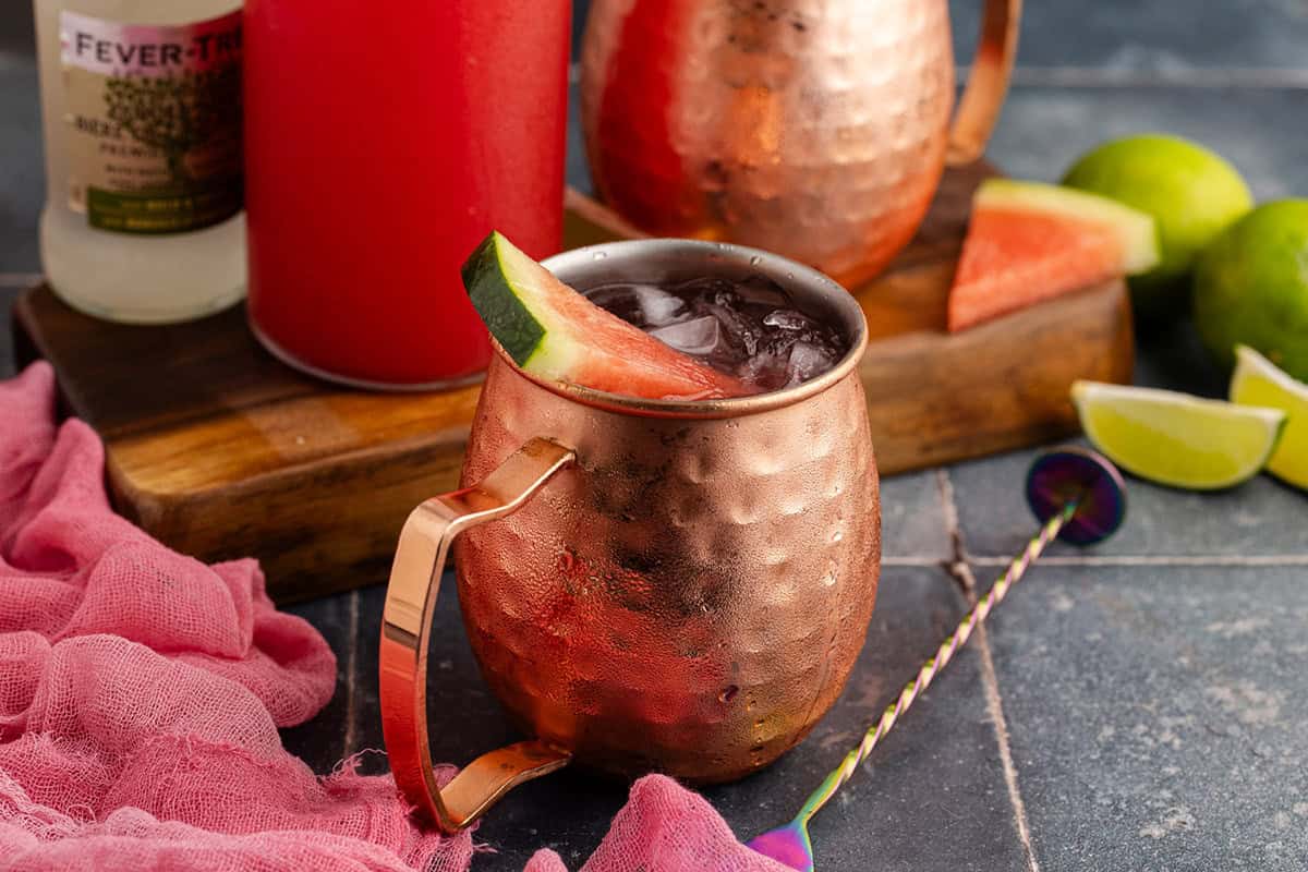 Watermelon Moscow Mule in Mule glasses with watermelon garnish with ingredients behind
