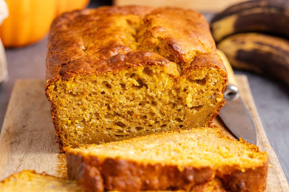 Pumpkin Banana Bread on a Cutting Board with bananas in the back