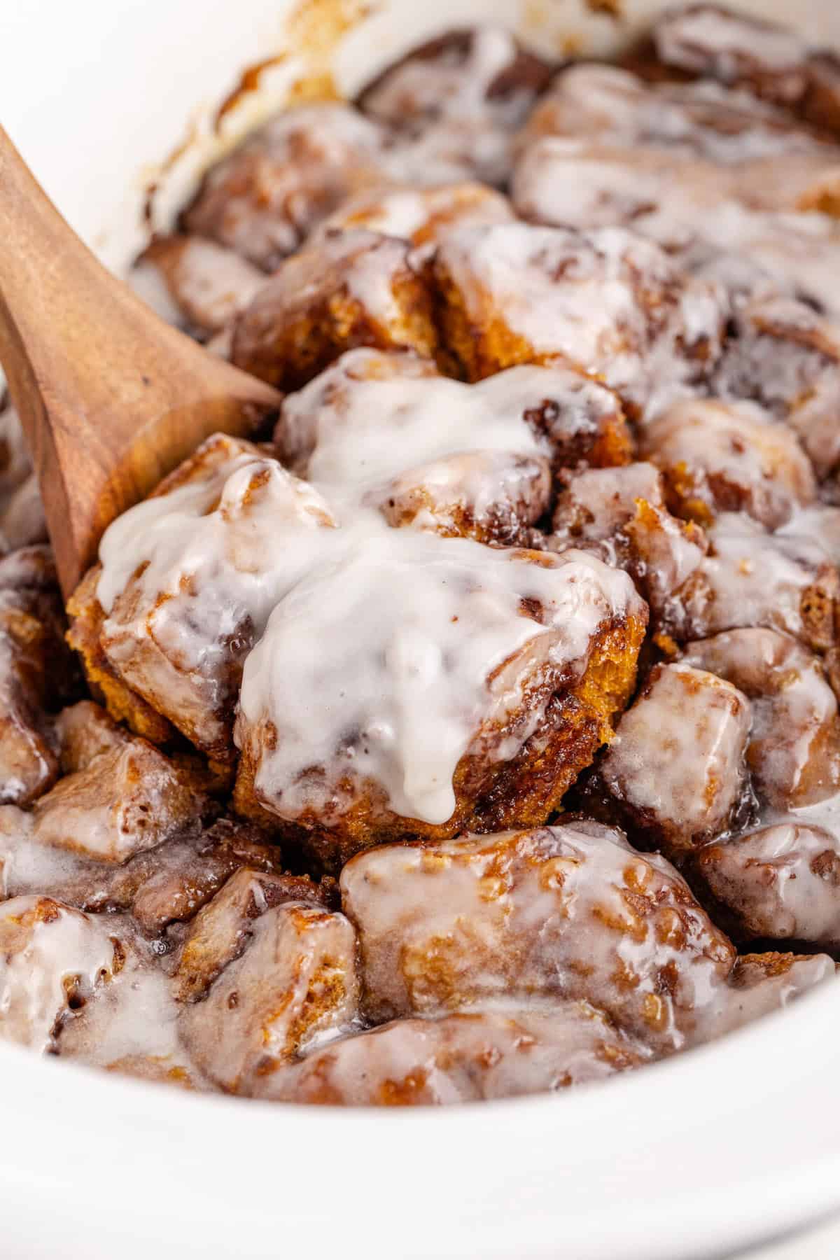 Crock Pot Cinnamon Bun Casserole Scooped from Crock Pot with Wooden Spoon
