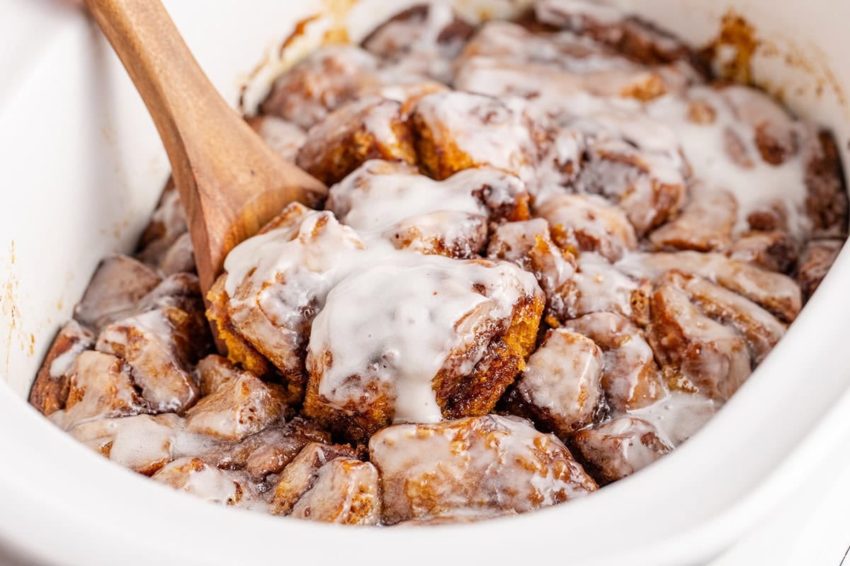 Crock Pot Cinnamon Bun Casserole Scooped from Crock Pot with Wooden Spoon