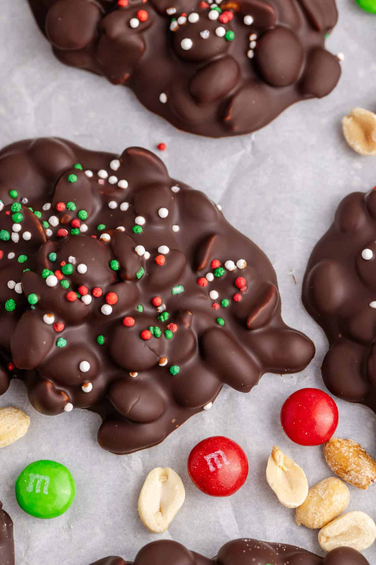Crockpot Candy Dark Chocolate Peanut Clusters with Sprinkles on Parchment Paper with M&Ms