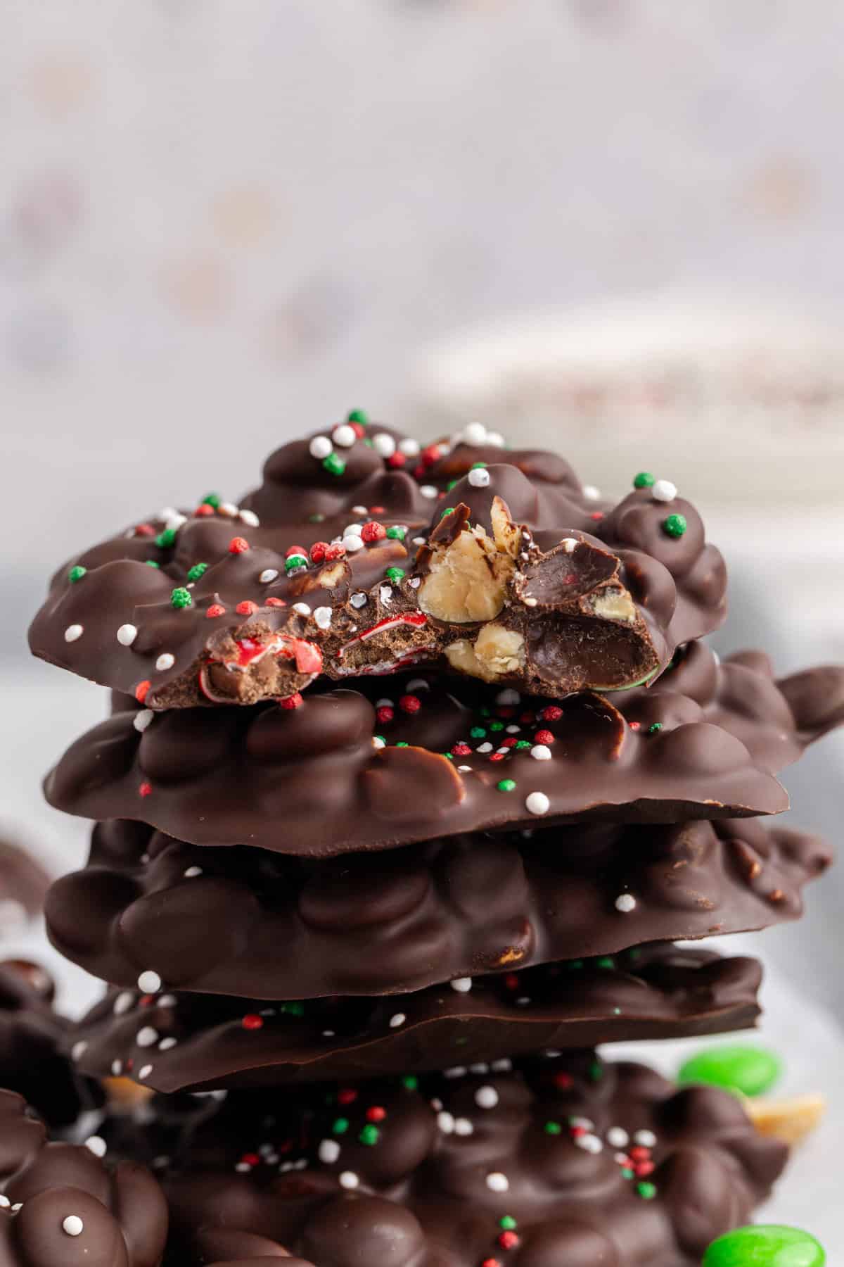 Crockpot Candy Dark Chocolate Peanut Clusters with Sprinkles Stacked with a Bite Taken