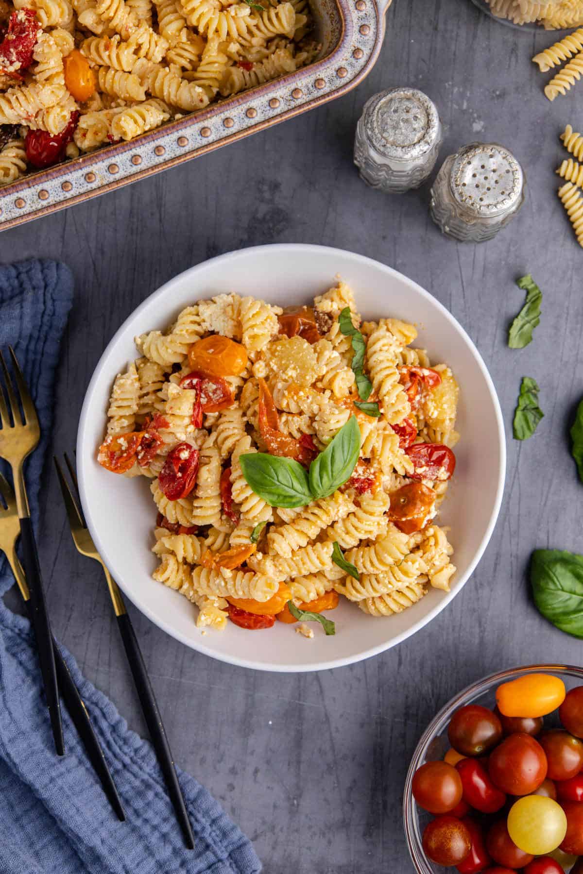 Feta Pasta Recipe Plated and Garnished with Fresh Basil Beside Casserole Dish and Fresh Tomatoes