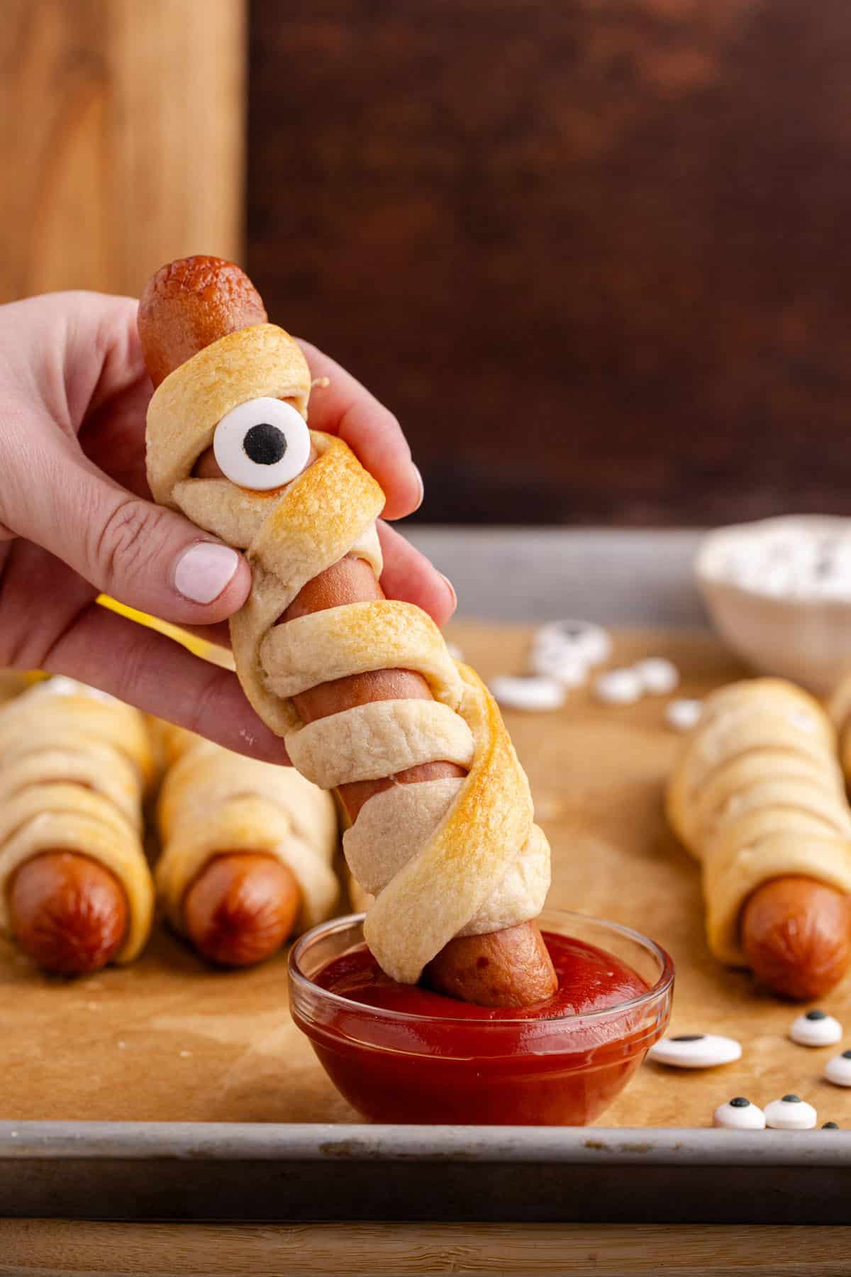 Hot Dog Mummy being dipped into ketchup with other mummy dogs in the back