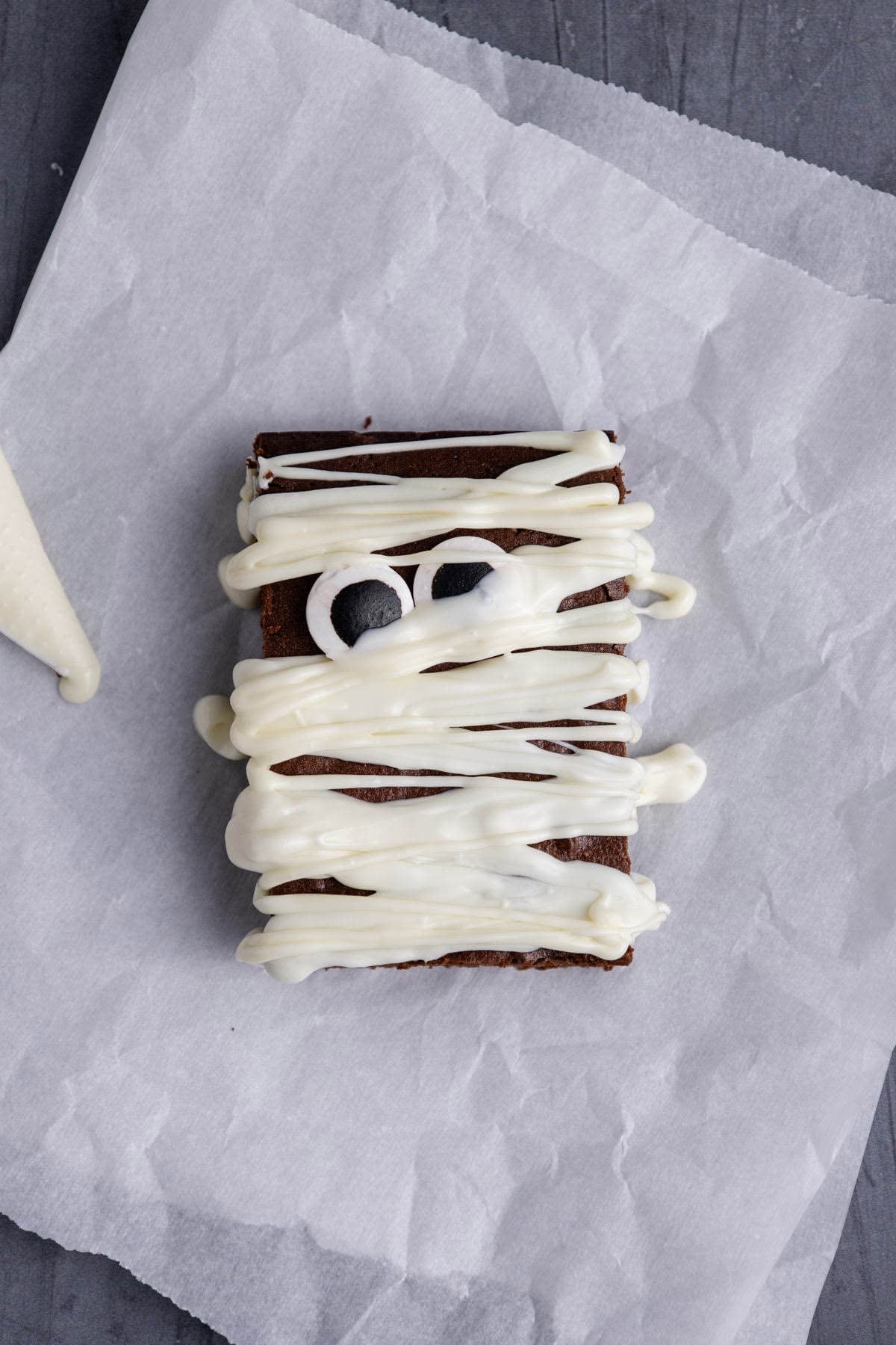Mummy Brownies laying flat on parchment paper with white chocolate in a piping bag