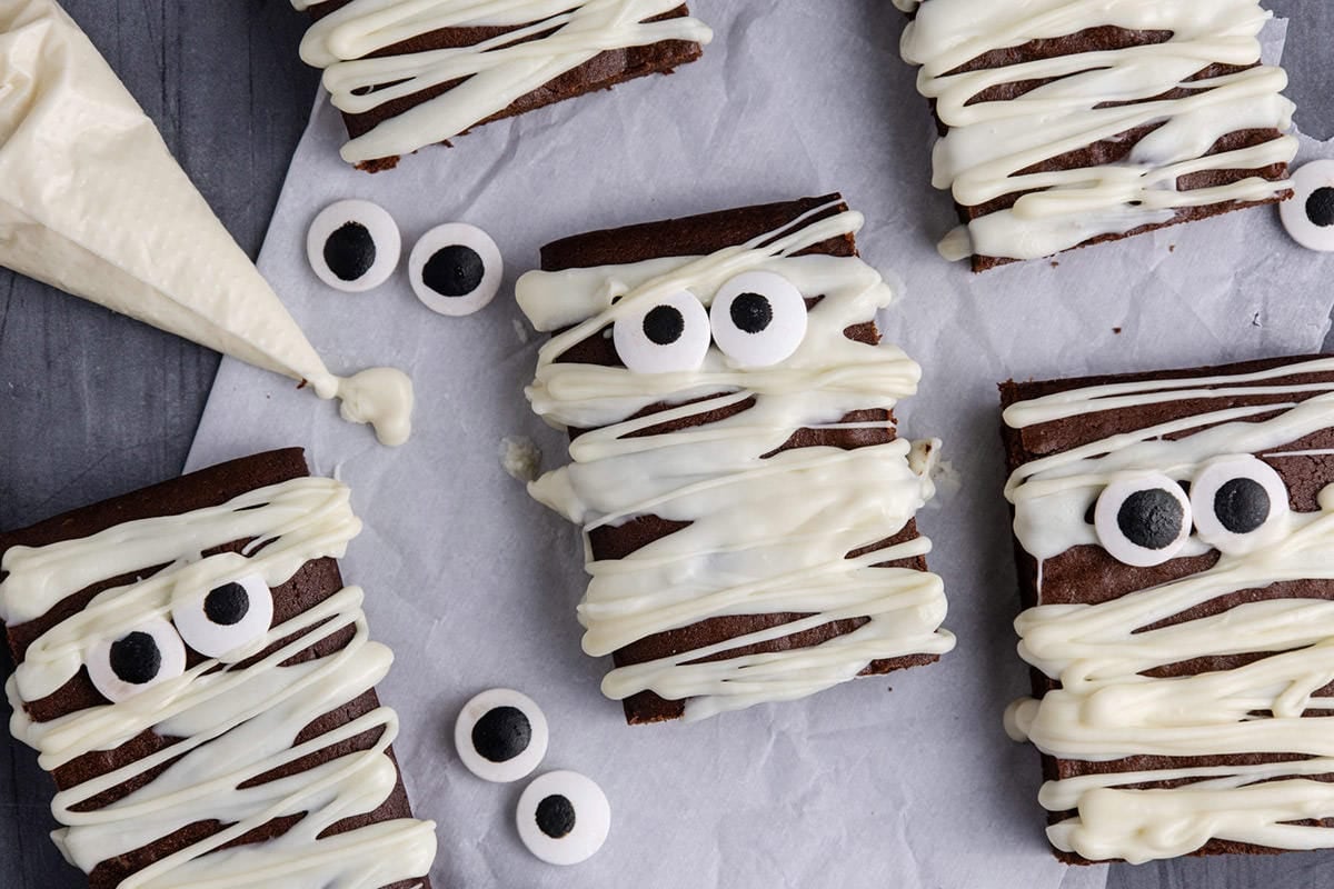 Mummy Brownies laying flat on parchment paper with white chocolate in a piping bag