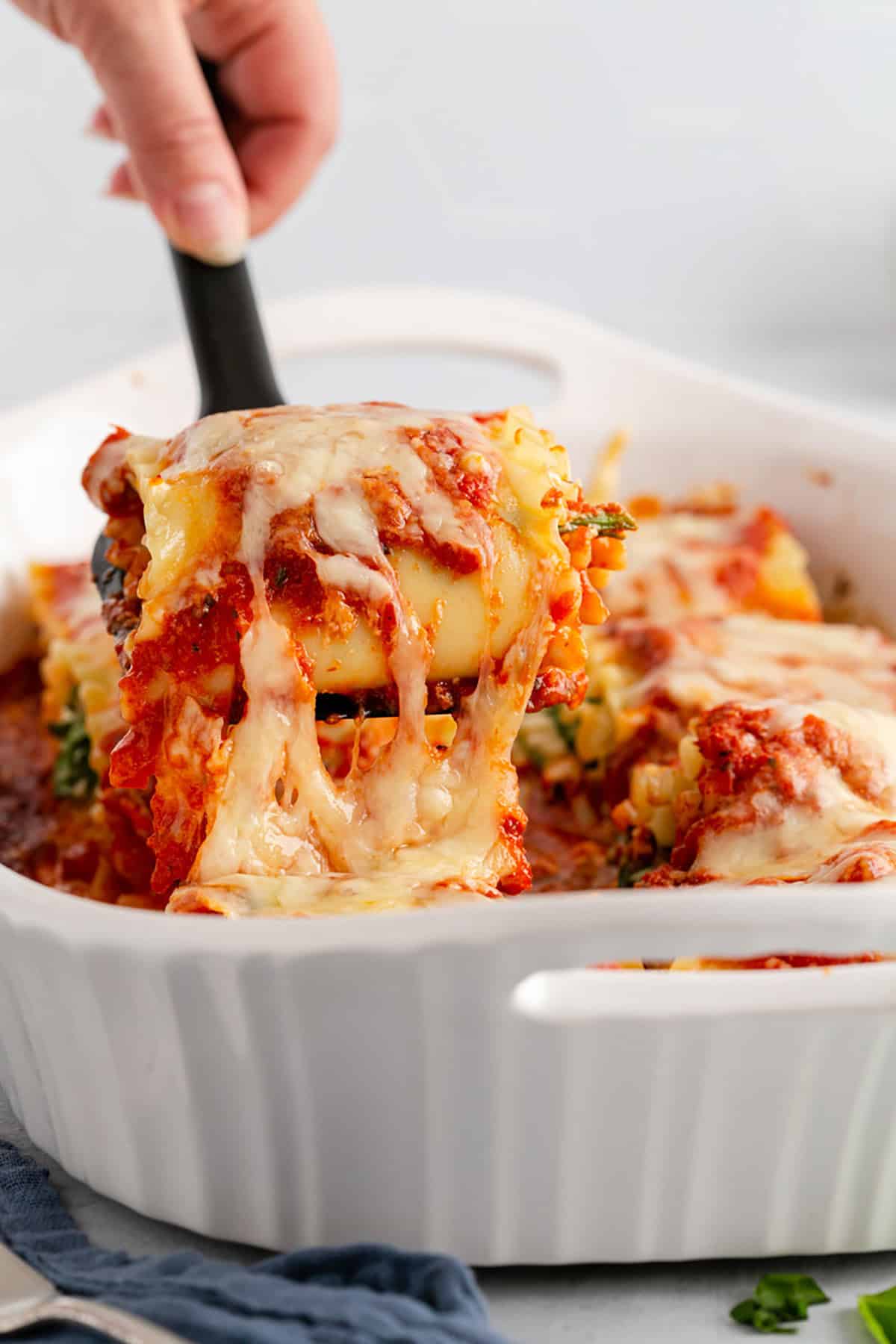 Spinach Lasagna Roll Ups Cheese Pull Being Lifted from the Baking Dish