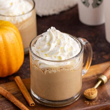 Starbucks Pumpkin Spice Latte on a cutting board with takeaway cups in the back