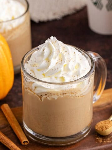 Starbucks Pumpkin Spice Latte on a cutting board with takeaway cups in the back