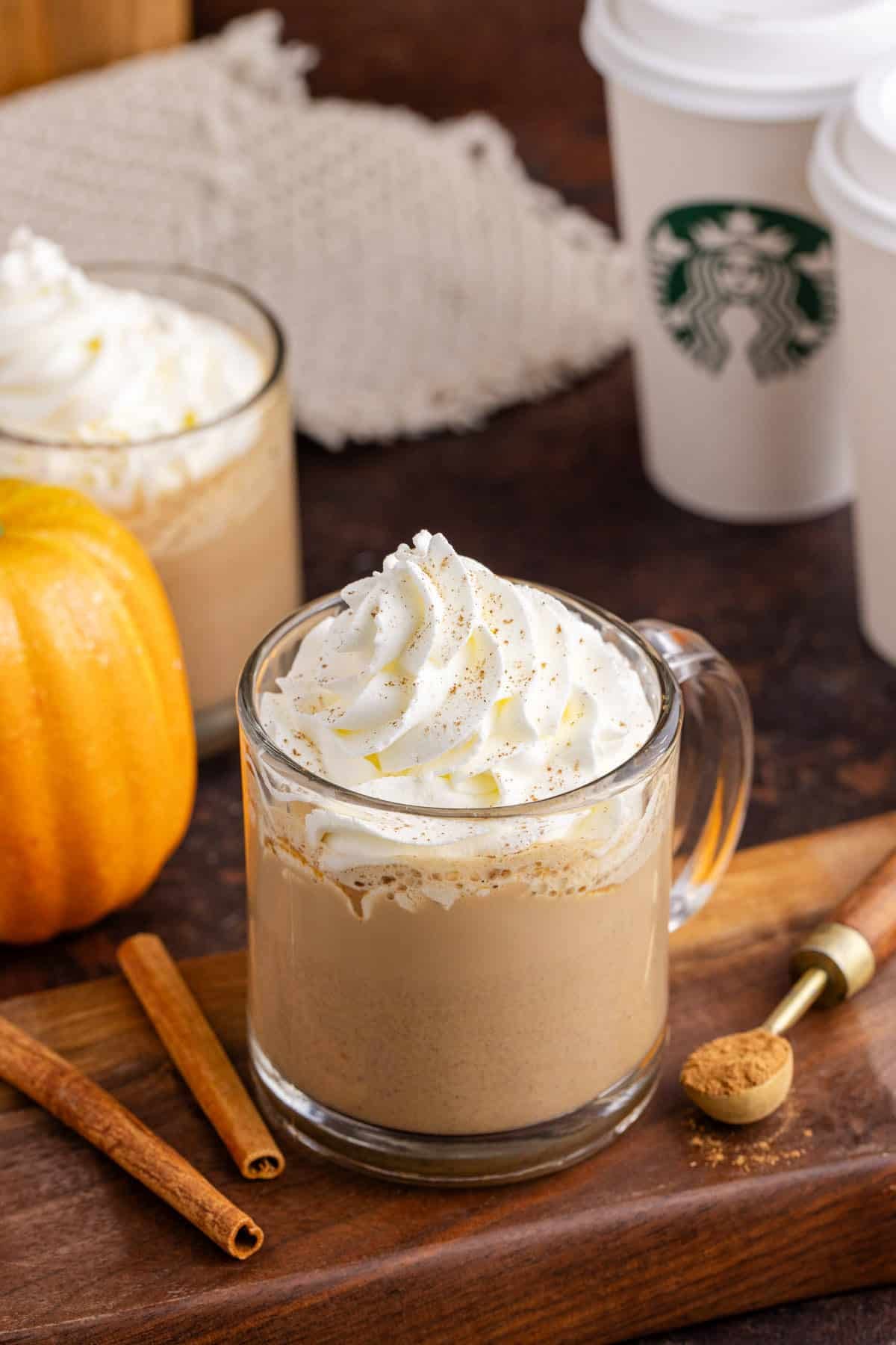 Starbucks Pumpkin Spice Latte on a cutting board with takeaway cups in the back