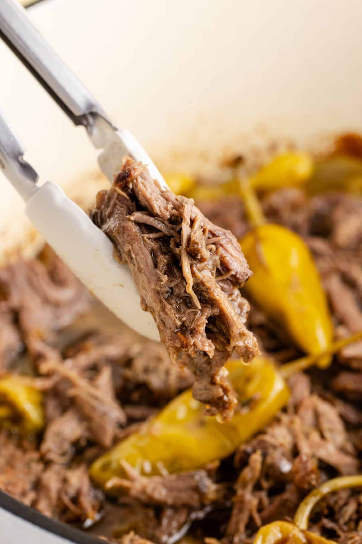 Mississippi Pot Roast shredded in a Dutch oven being picked up with tongs
