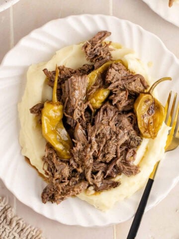 Mississippi Pot Roast shredded on top of mashed potatoes and peperoncino peppers