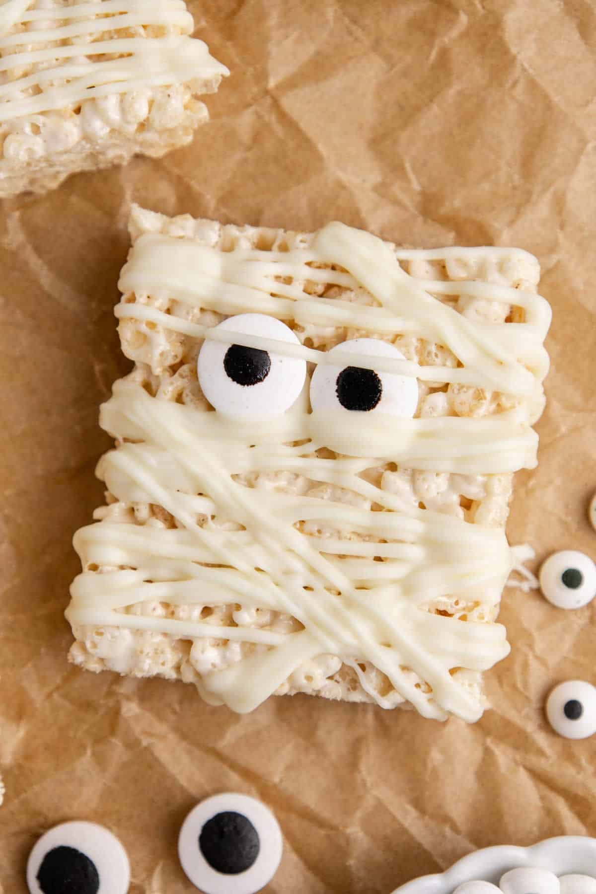 Mummy Rice Krispie Treats close up on parchment paper with candy eyeballs around it