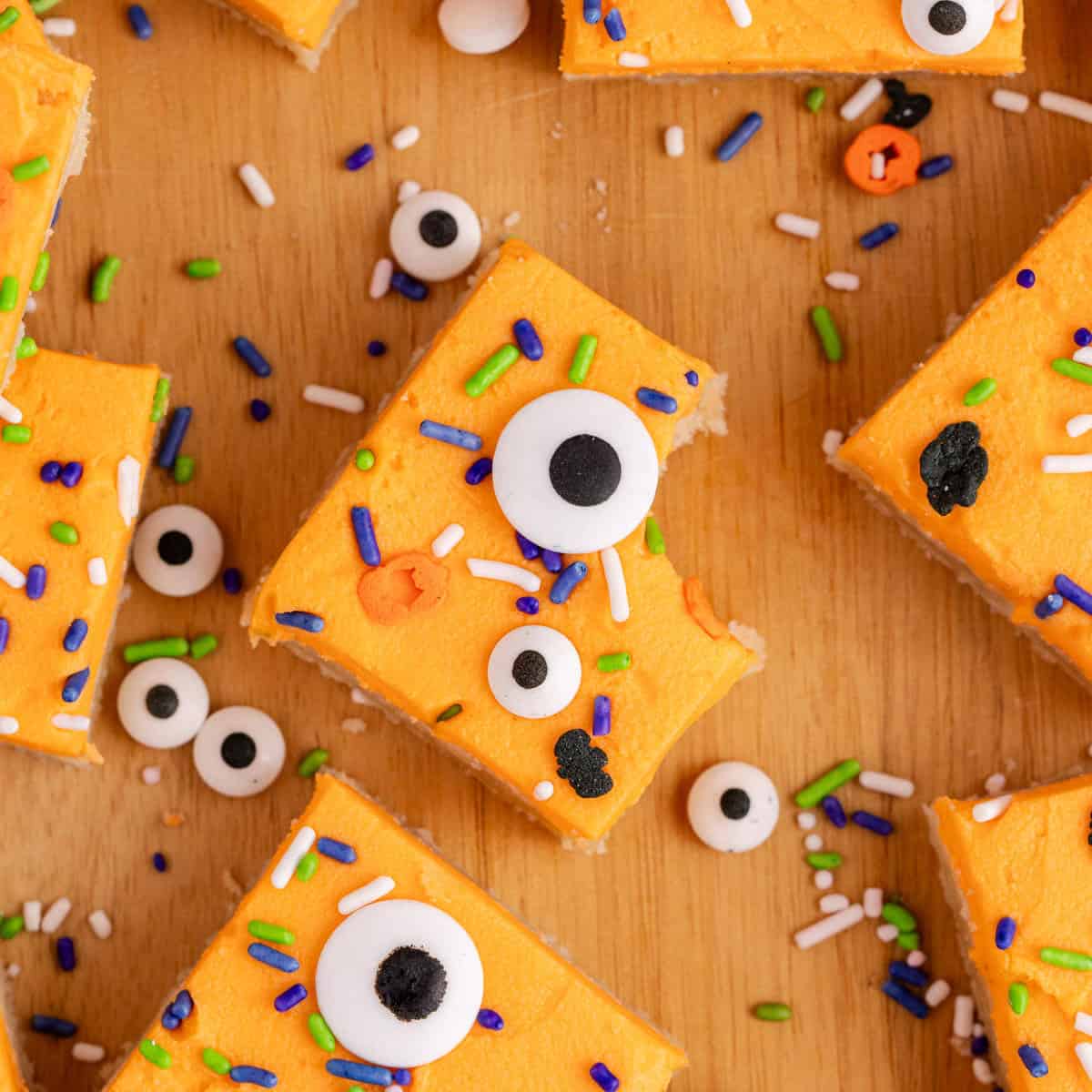 Sugar Cookie Bars with orange frosting and googly eyeballs on a cutting board