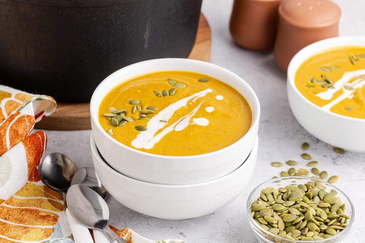 Pumpkin Carrot Soup in bowls with pumpkin seeds and drizzle coconut milk