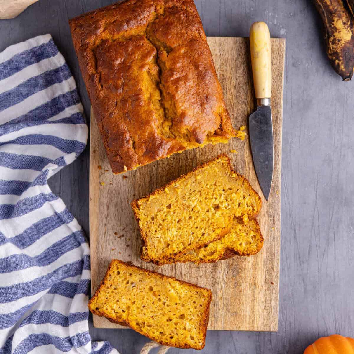 Pumpkin Banana Bread loaf on a cutting board with slices around it