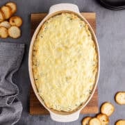 Baked Spinach and Artichoke Dip in Oval Baking Dish with Golden Cheese Top Layer and Crackers Beside