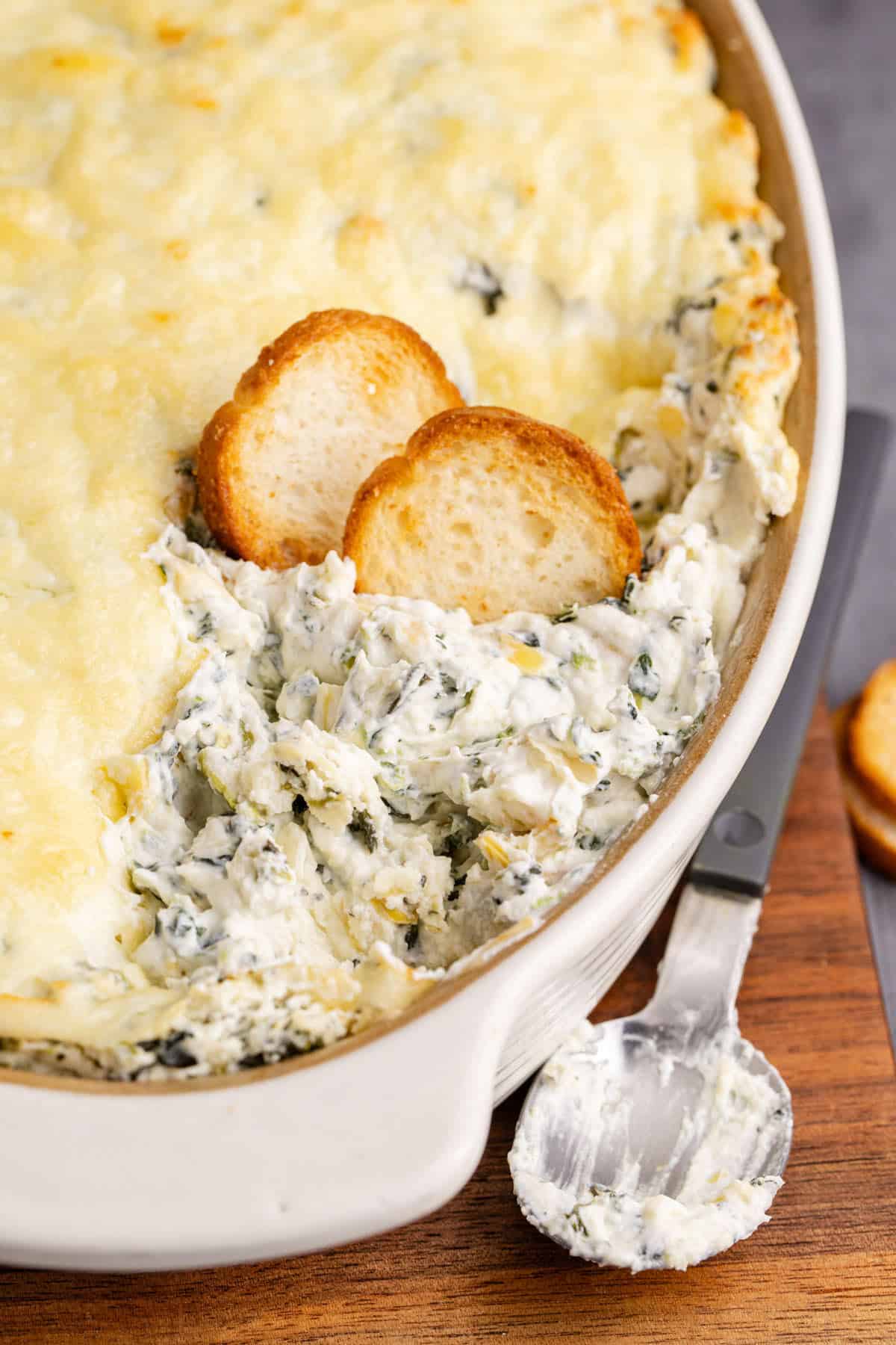 Baked Spinach and Artichoke Dip with Scoop Taken Out and Crackers for Dipping