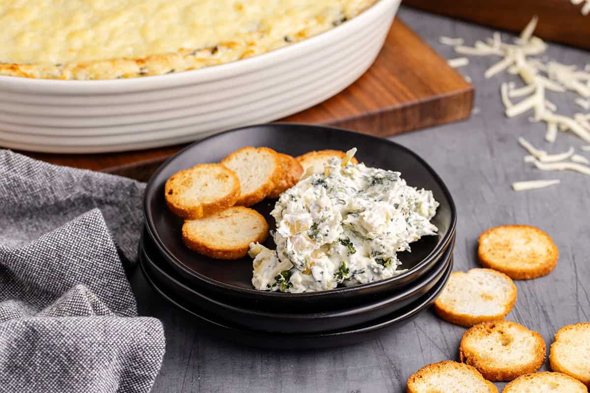 Baked Spinach and Artichoke Dip Scooped and Served on a Plate with Crackers