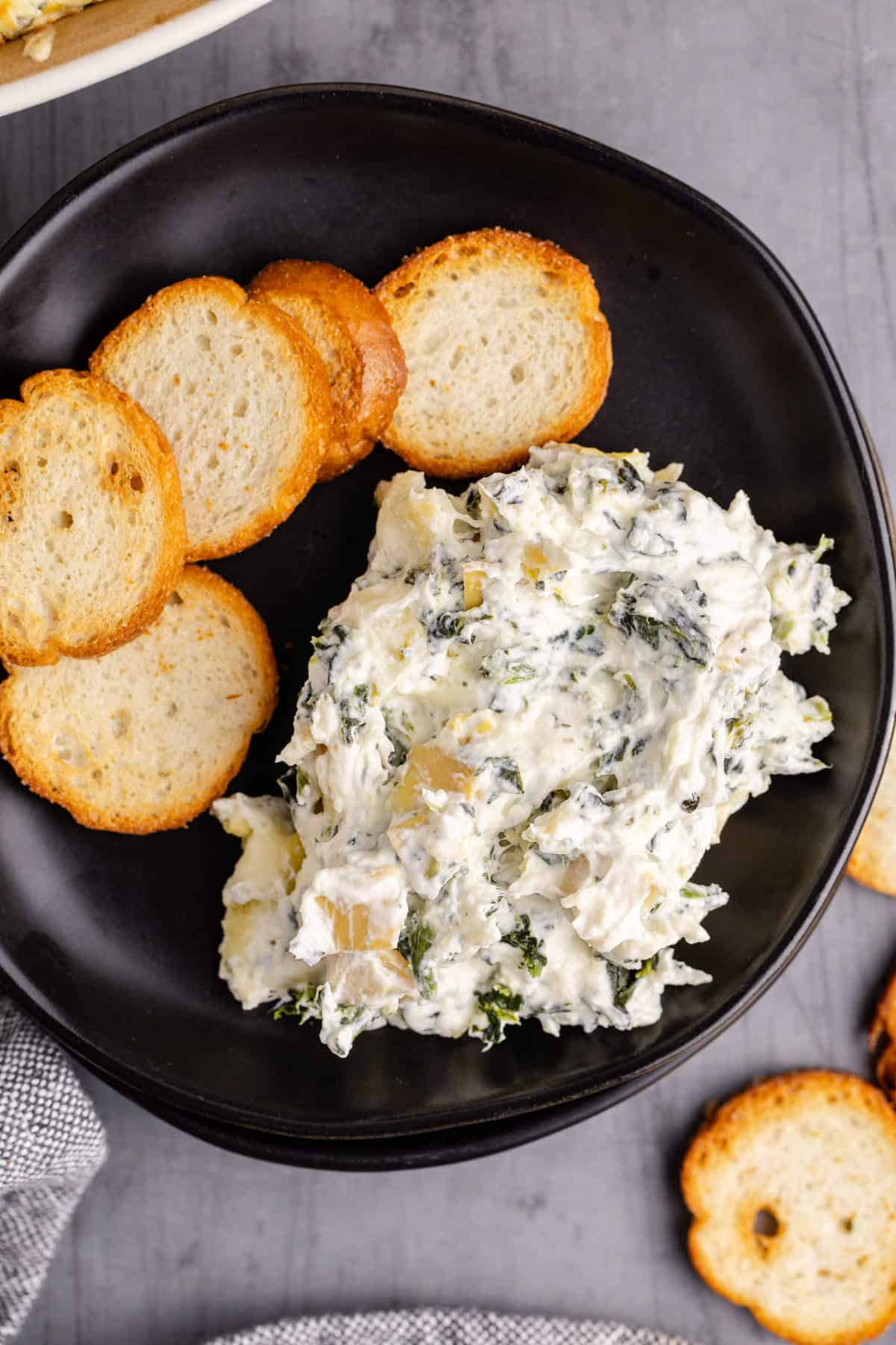 Baked Spinach and Artichoke Dip Scooped and Served on a Plate with Crackers