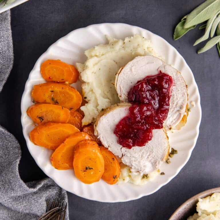 Sliced Boneless Turkey Breast Plated with Roasted Carrots Mashed Potatoes and Cranberry Sauce
