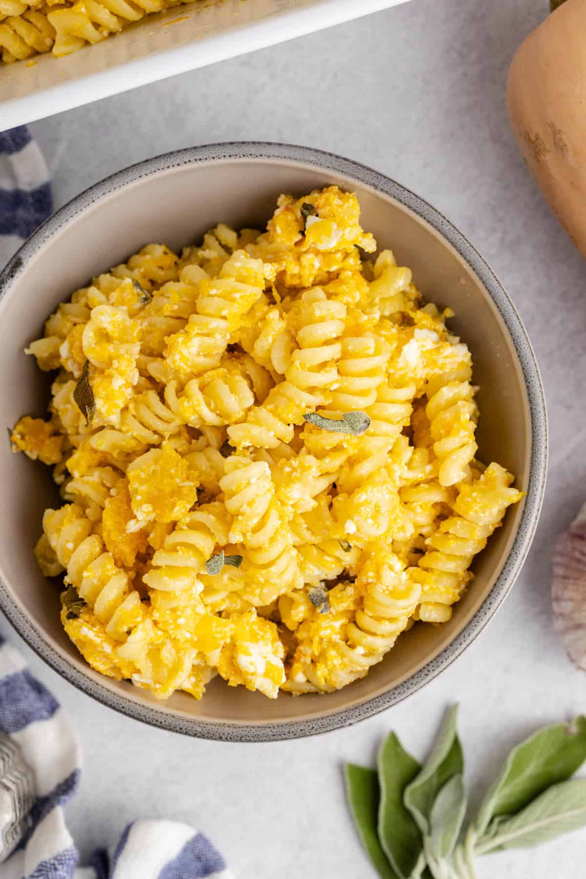 Butternut Squash Feta Pasta close up of a bowl with fresh sage and a garlic bulb beside