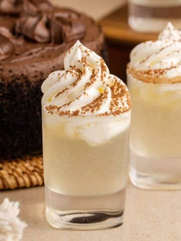 Chocolate Cake Shot in Shot Glasses and Garnished with Whipped Cream and Cocoa Powder with Chocolate Cake in Background