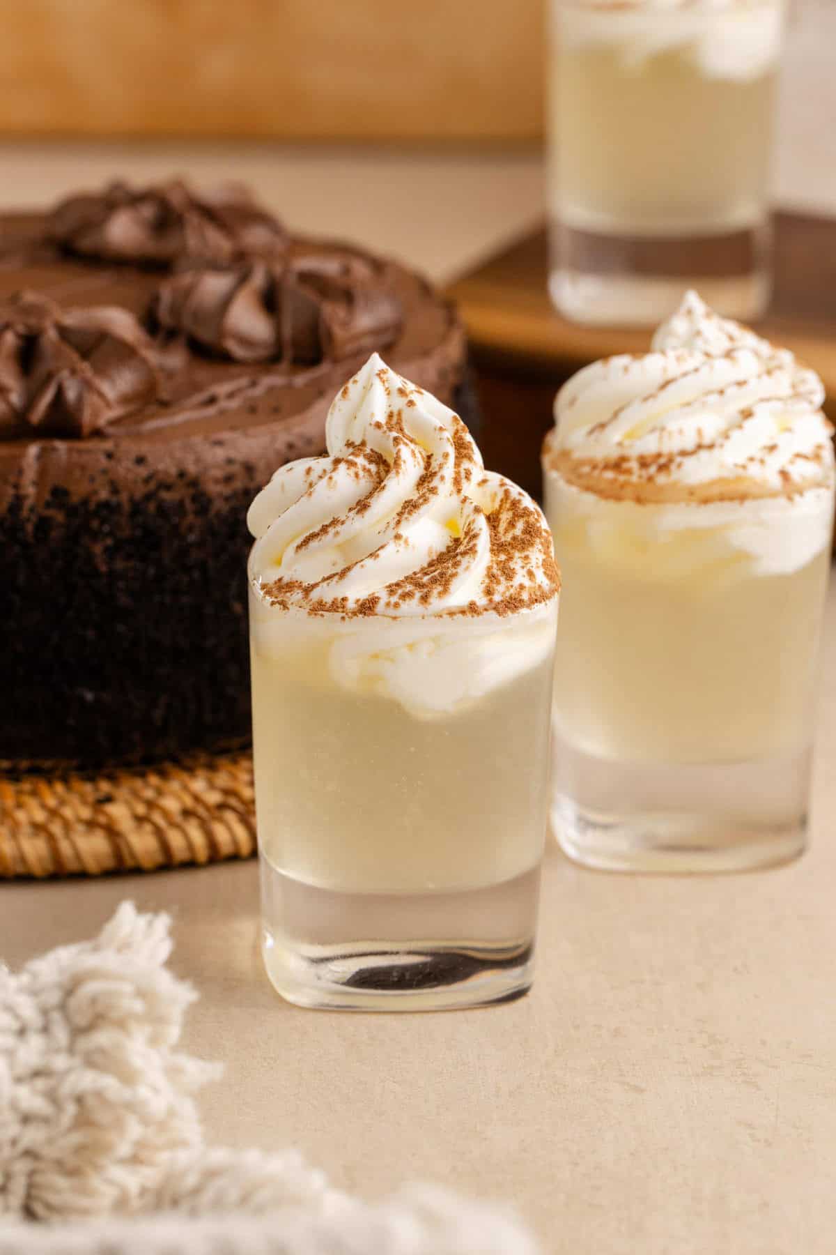 Chocolate Cake Shot in Shot Glasses and Garnished with Whipped Cream and Cocoa Powder with Chocolate Cake in Background