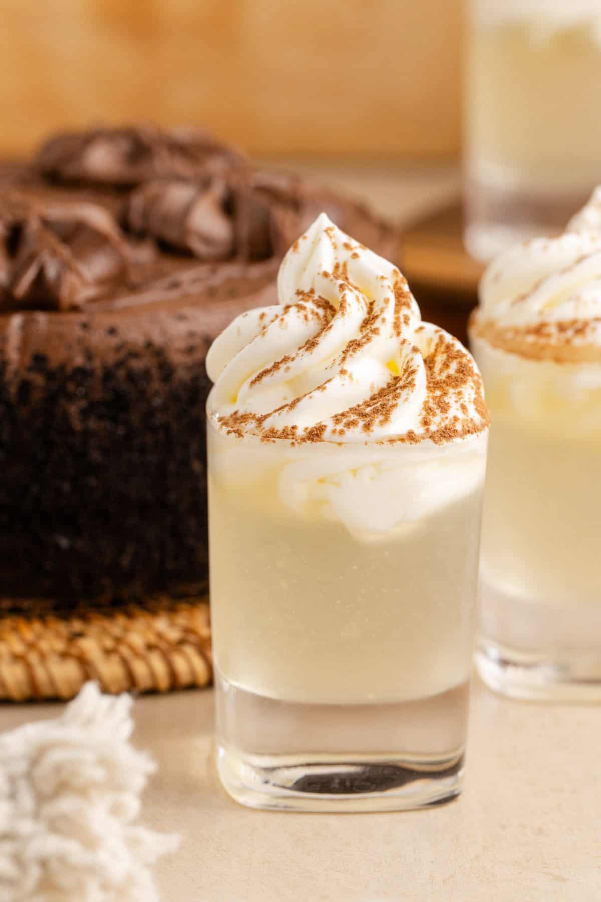 Chocolate Cake Shot in Shot Glasses and Garnished with Whipped Cream and Cocoa Powder with Chocolate Cake in Background