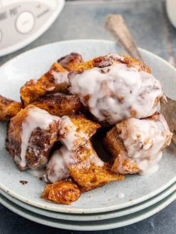 Crockpot Cinnamon Bun Casserole with Icing Served on a Plate with Crockpot in Background