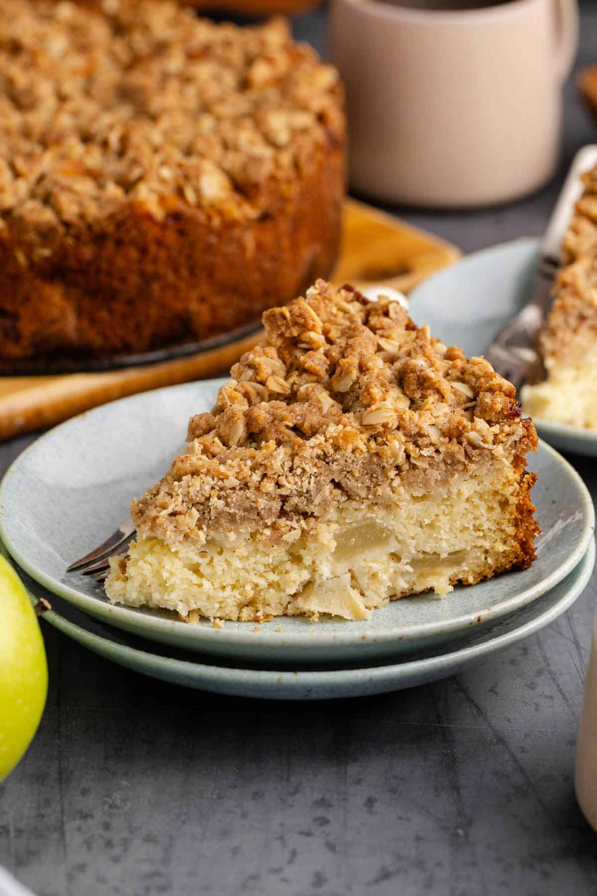 Slice of Apple Coffee Cake Served on a Plate with Full Cake in Background