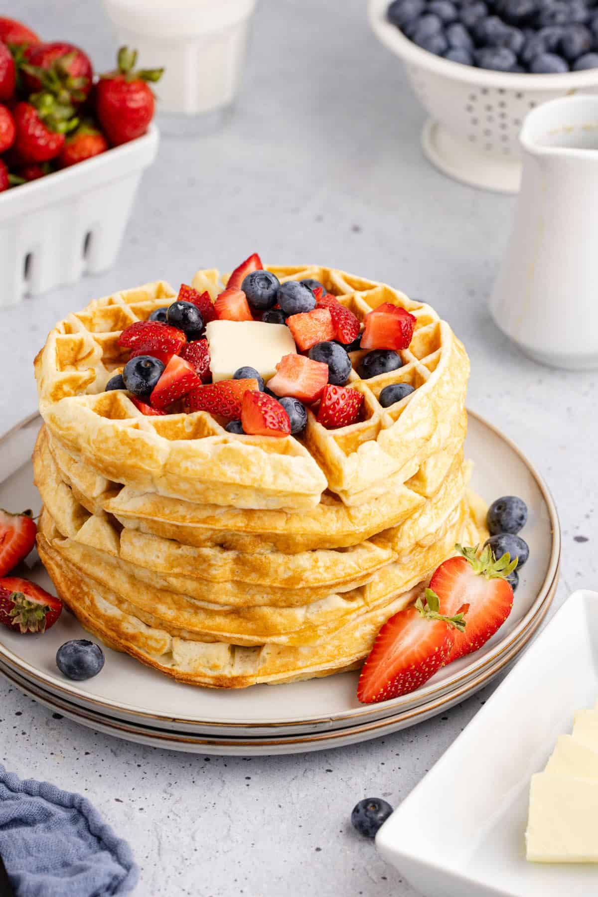 Stack of Gluten Free Buttermilk Waffles Topped with Berries and Pat of Butter Served on a Plate with Berries in Background