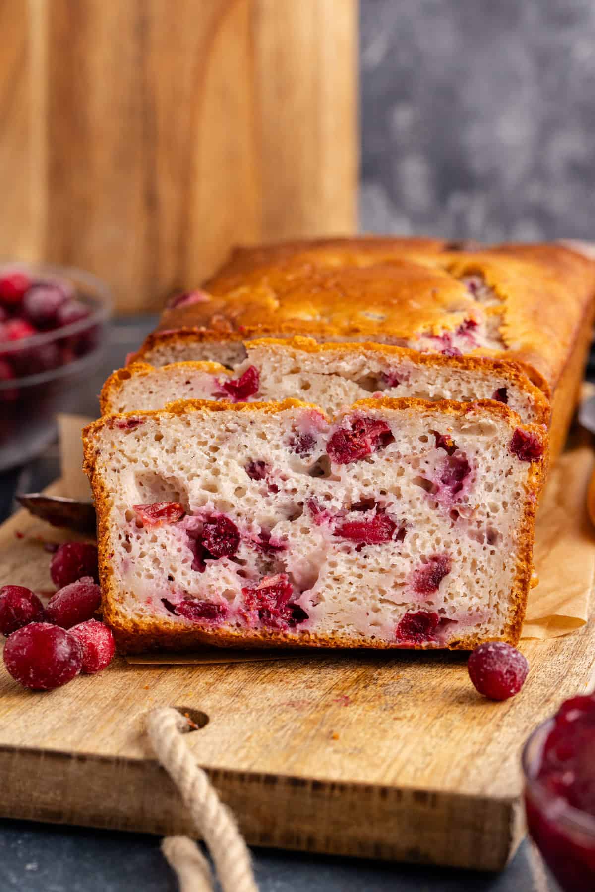 Cranberry Sauce Bread on a cutting board with frozen cranberries around