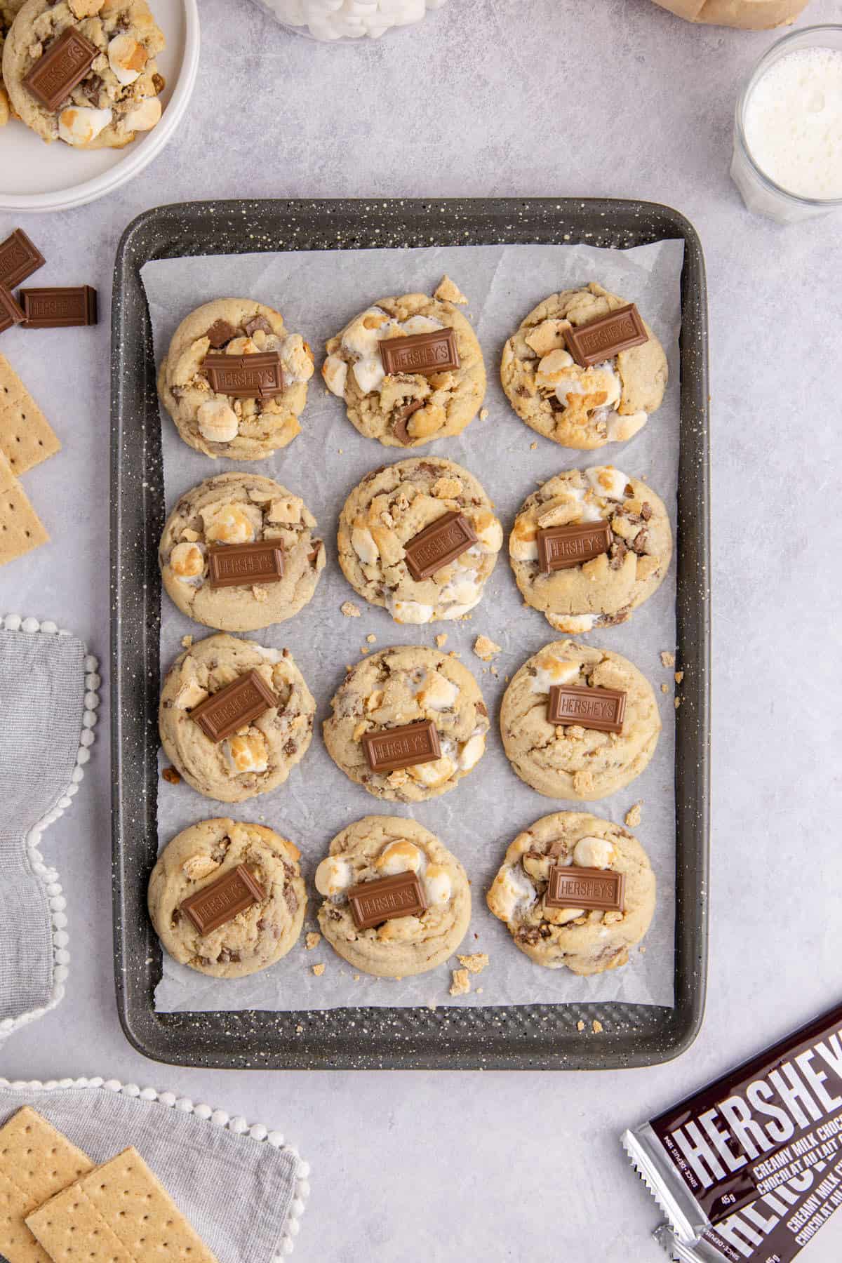 Smores Cookies baked on a cookie sheet with graham crumbs and a Hershey square on top