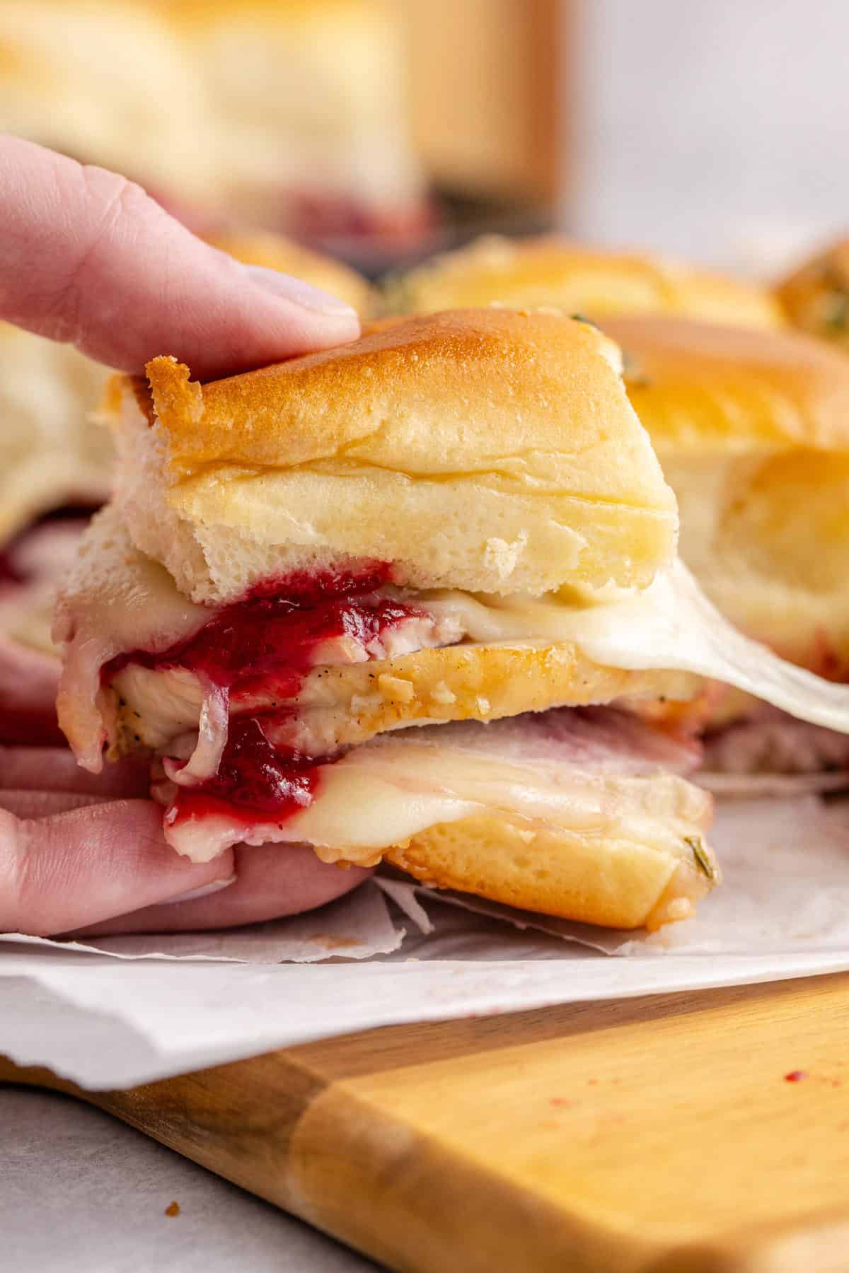 Hand Pulling Turkey Sliders on Hawaiian Rolls with Melted Cheese