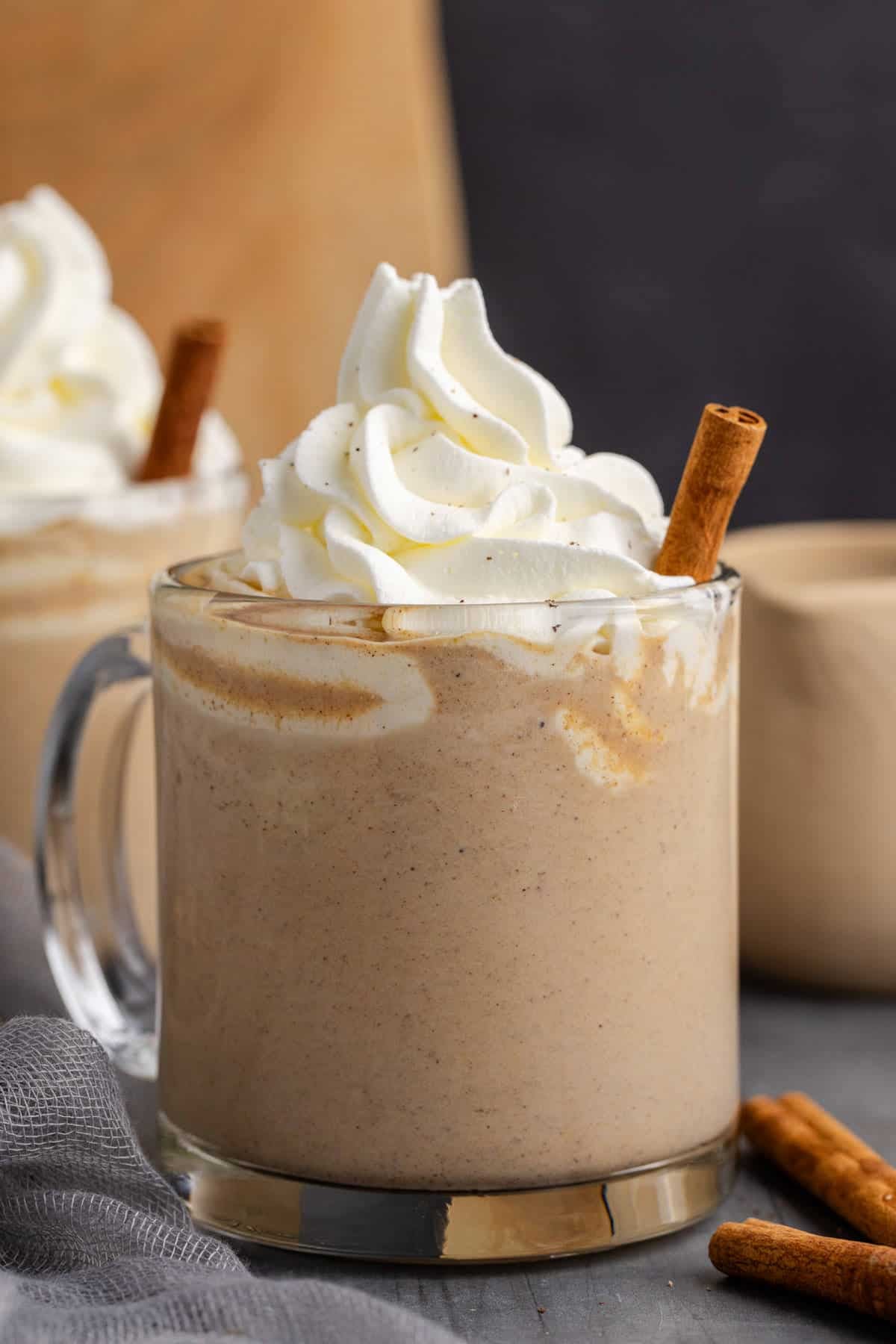 Pumpkin Chai Latte Served in Clear Mug with Whipped Cream and Cinnamon Stick Garnish with Cinnamon Sticks Around